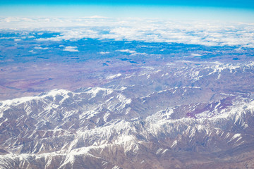 Mountains with snowy peaks from the window of an airplane on a sunny day.