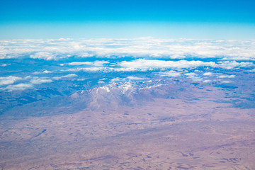 Mountains with snowy peaks from the window of an airplane on a sunny day.