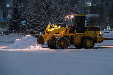 Wheel loader is removing snow at night during snowfall. Selective focus, blurred. Snow removing concept.