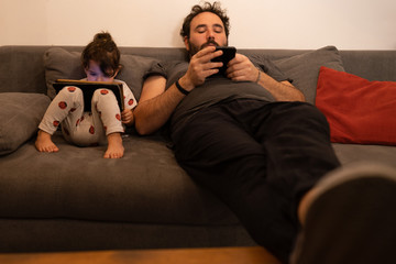 father and daughter with pacifiers on the sofa while using a tablet and a phone during quarantine