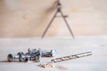 A drill, screws and a circle and pensil in the background placed on wooden board