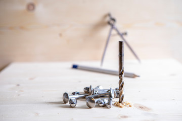A drill, screws and a circle and pensil in the background placed on wooden board