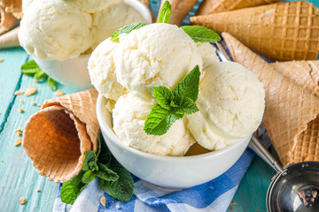 Homemade white vanilla ice cream balls with mint leaves in small portioned white bowl. With ice cream waffle cone and spoon,  on rustic turquoise wooden table, copy space