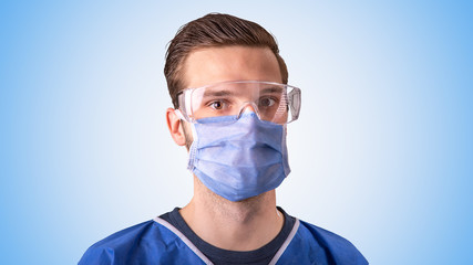 Arzt oder Pfleger mit Mundschutz und Schutzbrille vor hellblauem Hintergrund