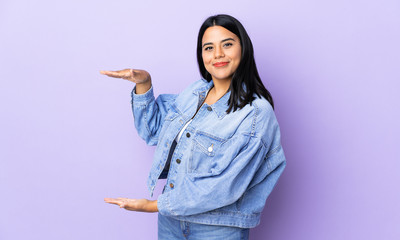 Young latin woman woman over isolated background holding copyspace to insert an ad
