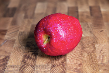 A close up to a fresh red apple on a wooden table. Water drops on the surface of the so called Christmas apple. Macro photography 