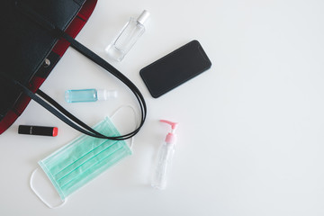 Flat lay of black leather women bag in outbreak situation open out with cosmetics, perfume, smartphone and antibacterial cleaners equipment to prevent Coronavirus or Covid-19 with copy space.