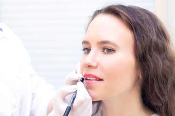 Young woman having permanent makeup on her lips at the beauticians salon. Permanent Makeup (Tattoo). drawing a contour with a white lip pencil