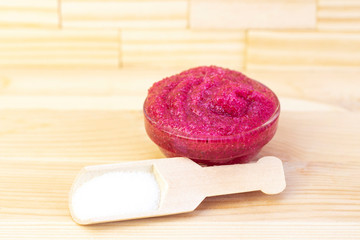 Natural pink body scrub made from sugar. Pink scrub in a glass cup on a background of candles and sugar.