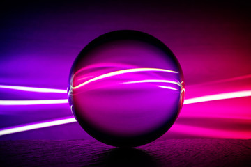 Crystal glass ball is lying on a stone surface on the colorful abstract background.