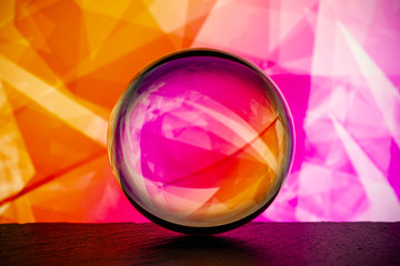 Crystal glass ball is lying on a stone surface on the colorful abstract background.