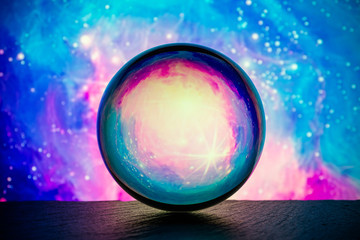Crystal glass ball is lying on a stone surface on the colorful abstract background.