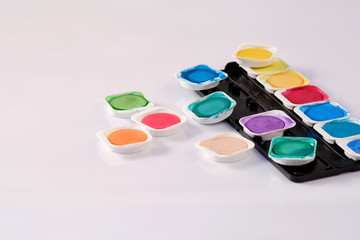 The bright variegated colours of a used watercolor box lying isolated on white background.