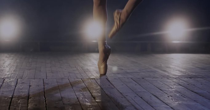 Close up of female legs of professional ballerina on pointe dancing on wooden floor in darkness. Practising and rehearsing classical ballet dance and pas. Art choreograpy concept.