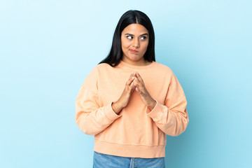 Young latin woman woman isolated on blue background scheming something