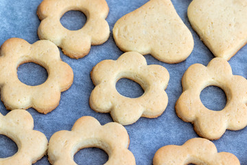 Baked shortbread cookies in the form of flowers and hearts on a baking sheet with parchment paper just taken out of the oven. Tea snack for breakfast. Selective focus. Closeup top view