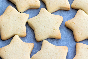 Baked shortbread cookies in the form of stars on a baking sheet with parchment paper just taken out of the oven. Tea snack for breakfast. Selective focus. Closeup top view