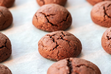 Baked cracked round chocolate cookies on a baking sheet with parchment paper just taken out of the oven. Tea snack. Selective focus. Closeup view