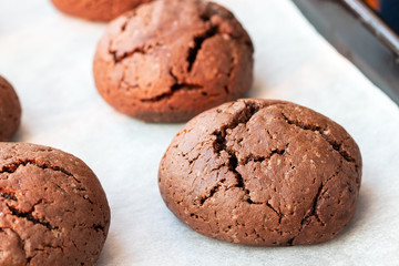 Baked cracked round chocolate cookies on a baking sheet with parchment paper just taken out of the oven. Tea snack. Selective focus. Closeup view