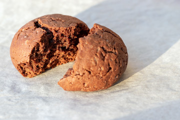 Baked cracked round chocolate cookie broken in half on a baking sheet with parchment paper just taken out of the oven. Tea or coffee snack. Selective focus. Closeup view