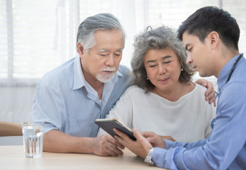 Caucasian doctor use tablet and talk with old asian female patient about disease symptom, elderly health check up at home.