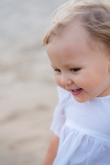 Toddler blonde in a white dress runs on the waves of the sea and laughs at sunset. Blur, high key, upper half. Blurred.
