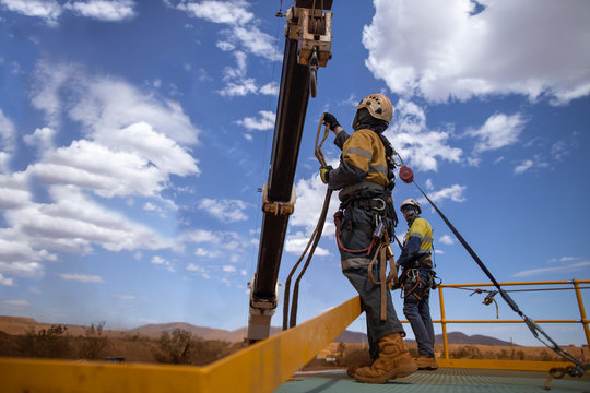 Safe workplace rigger wearing working at heights harness having clipping an inertia reel shock absorbing hook fall arrest device on the back safety harness hook while working from exposure open edges 