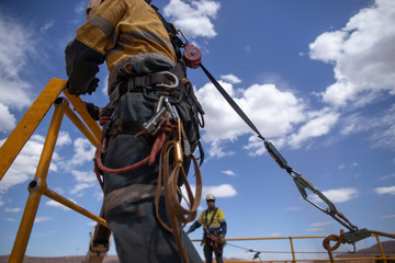 Safe workplace rigger wearing working at heights harness clipping an inertia reel shock absorbing...