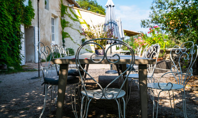 Flowery farm backyard with table and chairs at sunny summer day. Open summer patio with white wrought iron furniture.