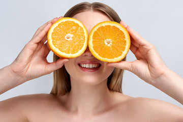 Pretty charming joyful attractive cheerful funny comic positive nude natural pure girl having two pieces of orange, on blue background. . Skincare. Vitamin C.