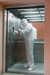 Coronavirus infection. Paramedic in protective mask and costume disinfecting an elevator with sprayer,