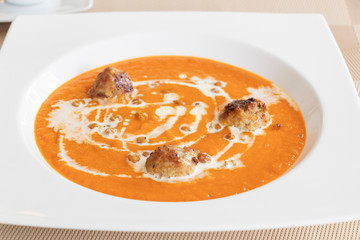close up of sweet chili and corrot soup served with meat ball topping with white cream. 