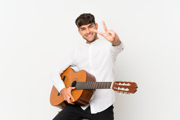 Young handsome man with guitar over isolated white background smiling and showing victory sign