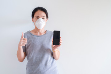 Asian young woman using smart phone wearing face mask protect air pollution,particulates and for protection flu.One hand home phone and other hand with yeah and happy look at phone,Health care concept