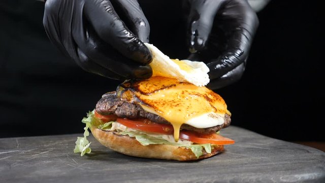 SLOW MOTION FOOD concept. Chef making burger. Close-up. Burger restaurant menu cooking process. Chef prepares fast food at restaurant putting fried egg on grilled meat. Full hd