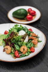 shrimp salad on a white plate with avocado red tomato and on a dark wooden background