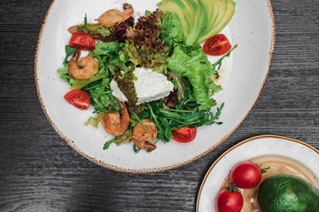 shrimp salad on a white plate with avocado red tomato and on a dark wooden background