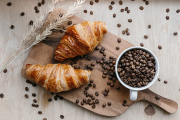 Cup full of coffee beans, two croissants and spica on wooden board