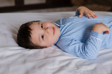 Happy baby boy in blue pajamas lies on the bed of the house, view from above, space for text