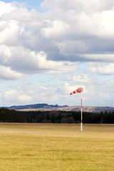 Red and white windsock on empty grassy airfield, dramatic clouds in background, windy weather...