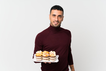 Young man over isolated white background holding mini cakes