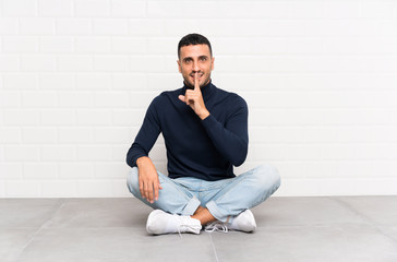 Young handsome man sitting on the floor doing silence gesture