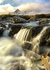 Flowing Waterfall In Sligachan With Morning Sunlight And Scottish Snowcapped Mountains In Background. Isle Of Skye, UK.