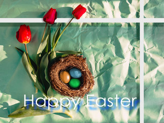 Multi-colored Easter eggs in a nest, red tulips and the inscription Happy Easter. Easter card.