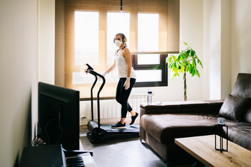 A girl with mask and gloves slim athlete does exercise at home running on the treadmill. Workout.