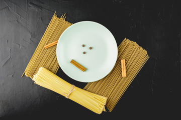 green ceramic plate with cinnamon and allspice and spaghetti on a soft-blurred textured black background