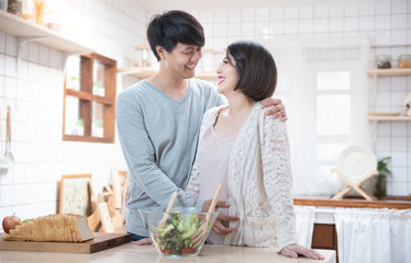 Asian man and pregnancy woman stand in kitchen at home.Father stand and look mother tummy mix salad feeling love expecting about future newborn baby. Love and care of pregnant mother’s day concept.