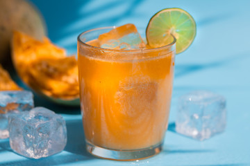 exotic fruit juice from Bel fruit or wooden Apple called in India Bel Ka Sharbat. cold fruit drink with ice on a blue background brightly lit by sunlight with a shadow from palm leaves