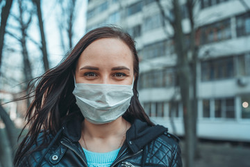 Portrait of young woman in medical mask on her face standing on street. Adult female covered her face with mask to protect yourself from diseases.