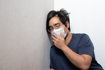 Male Asian young man wearing surgical mask feeling sick headache and coughing leaning on wall isolated on white background.Wuhan coronavirus (COVID-19) outbreak prevention. Health care concept